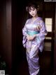 A woman in a purple kimono standing in front of a door.