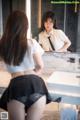 A woman in a white shirt and black skirt looking at herself in the mirror.