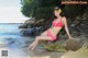 A woman in a pink bikini sitting on a rock on the beach.