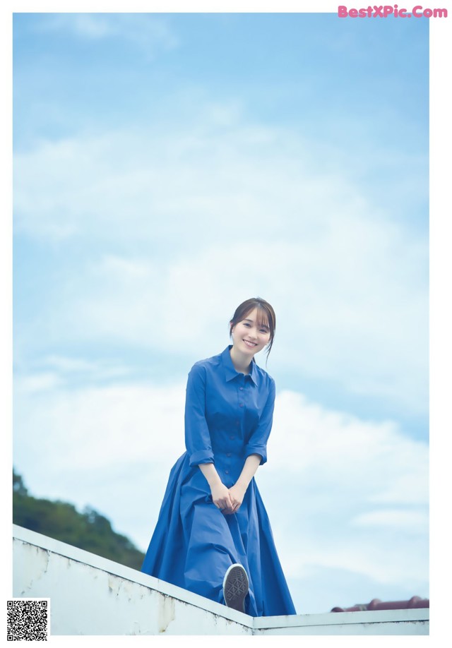 A woman in a blue dress standing on top of a building.