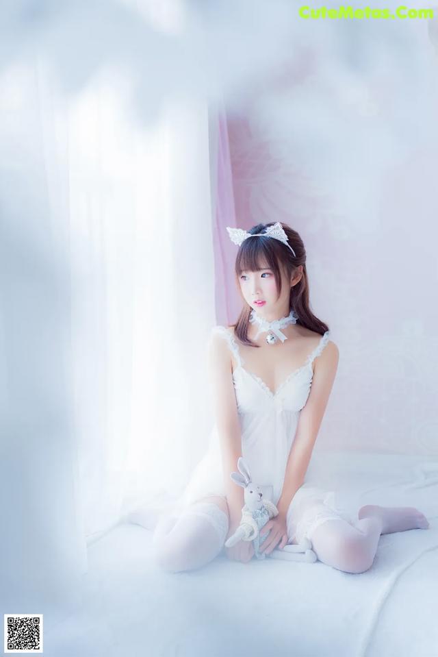 A woman in a white dress sitting on a bed.