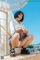 A woman in a white shirt and gray skirt sitting on a ledge.