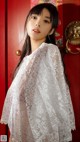 A woman wearing a white lace shawl standing in front of a red door.