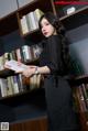 A woman standing in front of a bookshelf holding a book.