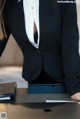 A woman in a black suit sitting at a desk with a laptop.