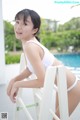 A woman in a white bathing suit sitting on a white chair.